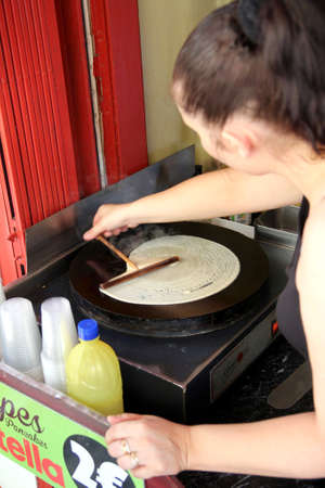 Carcassonne, Languedoc-Roussillon, France - August 24 2017: A young French woman making a traditional French crepe, or pancake, by rolling out the batter with a wooden spreaderのeditorial素材
