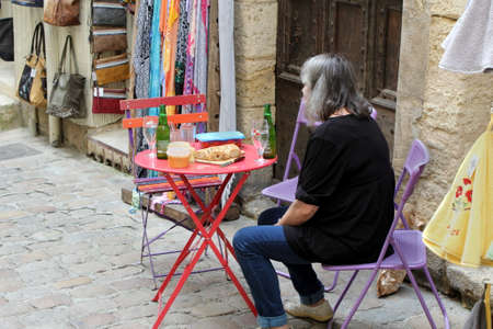 Pezenas, Herault, France - Aug 26 2017: Older woman sitting down at an outside table to enjoy lunch and a bottle of beerのeditorial素材