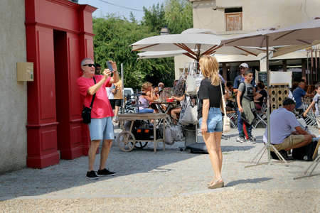 Carcassonne, Languedoc-Roussillon, France - August 24 2017: Middle aged man taking a phone photograph of an attractive woman tourist in a busy town square in Carcassonne, Languedoc, Franceのeditorial素材