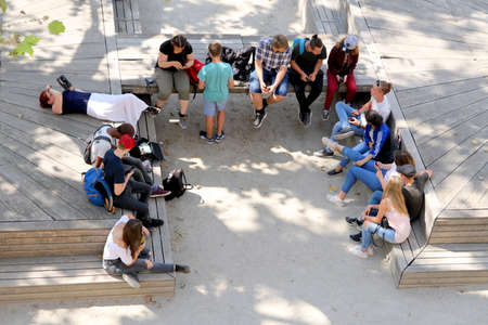 Carcassonne, Languedoc-Roussillon, France - August 24 2017: Overhead view of a group of teenagers relaxing on wooden benches, talking and using mobile phones and tabletsのeditorial素材