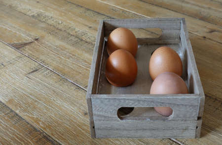 Four brown eggs in a wooden box with space for six eggs, in natural light.の写真素材