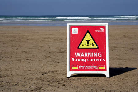 Perranporth, Cornwall, UK - April 9 2018: RNLI Lifeguard sign on a wide deserted beach, warning of...