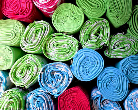 Overhead view of rolled up beach mats, mostly green, blue and red, in abstract background pattern.