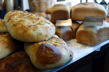 Shallow focus close up of rosemary and garlic focaccia bread, with other loaves in blurred background.の写真素材