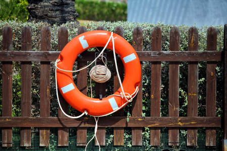 Bright red lifebelt, or life preserver buoyancy aid, attached to a wooden fence outside in bright...