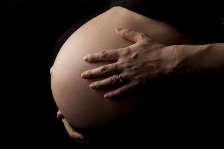 close up of a pregnant womans stomach, isolated on black background.の写真素材