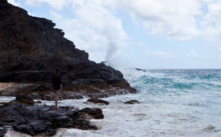 A young woman watches the Halona Blow Hole on the shore of Oahu, Hawaii の写真素材