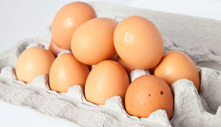 A dozen eggs in their carton on a white background