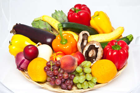 A number of fresh fruits and vegetables in a wicker basket on a white background の写真素材