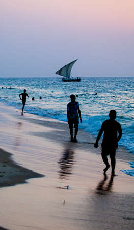 A group of teenagers frolick in the surf in Stonetown, Zanzibar, Tanzania. A dhow crosses the horizon behind.の写真素材
