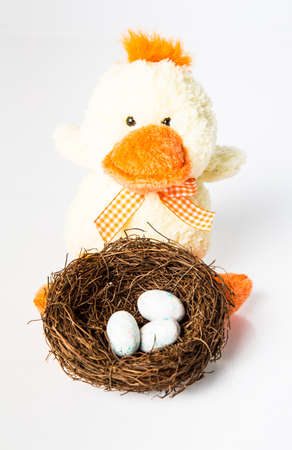 A stuffed toy duck and a nest full of candy eggs. Easter Concept. Isolated on white.