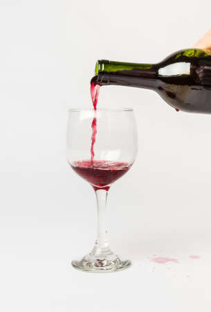 Red Wine pouring out of a bottle into a glass and splattering the white background.の写真素材
