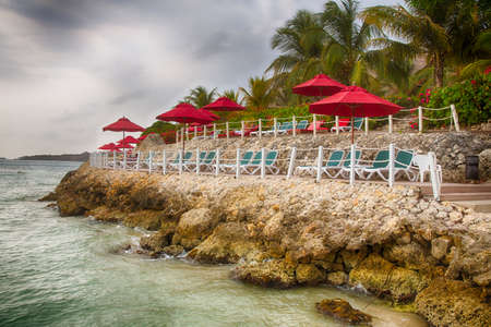 Lounge chairs under red umbellas on the lounge deck of a Caribbean beach front resort.の写真素材