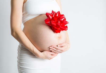 A pregnant woman cradels her baby belly with  gift bow attached.の写真素材