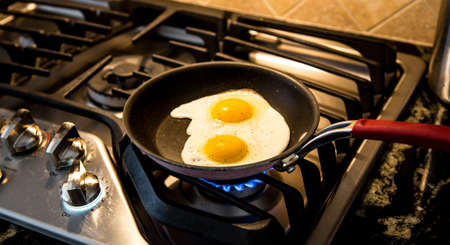 Two eggs being fried in a non-stick skillet on a gas range.の写真素材