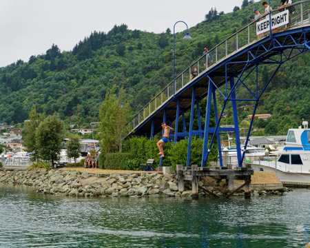 Picton, Marlborough Sounds/New Zealand - February 1, 2020: Young man jumps off the Marina footbridge into the sea beneath, while onlookers film the jump. Picton Marina, Marlborough Sounds, New Zealand.のeditorial素材