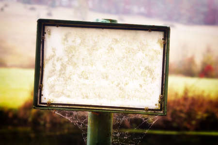 Empty, damaged white sign standing on a dirty pole with spiderweb - no text, lots of copy space.の写真素材