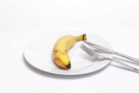 Banana and cutlery on a white dish against white background. Helathy, vegan food concept.の写真素材