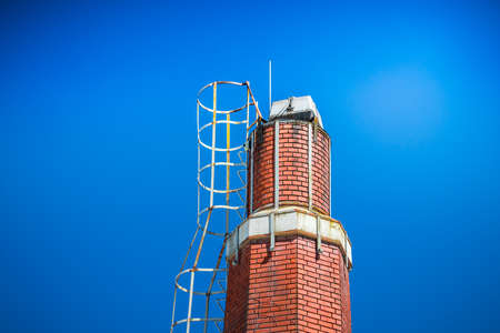 Old orange red brick chimney against blue sky.の写真素材