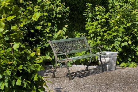 Green metal bench, standing in a park on a hedge, peaceful resting place の写真素材