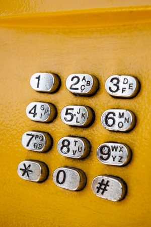 Metal keypad with numbers, part of yellow public phone on the street 