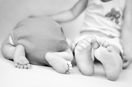 Little girl is comforting her baby brother. Black and white photo with soft focus on their feet.の写真素材