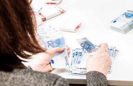Successful business woman is counting money bills ona a desk. Isolated on white. A woman is counting savings in euro currency on a white table.の写真素材