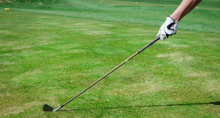 A hand is holding a golf club and measuring the Trajectory. Green grass, white glove with shallow depth of fieldの写真素材