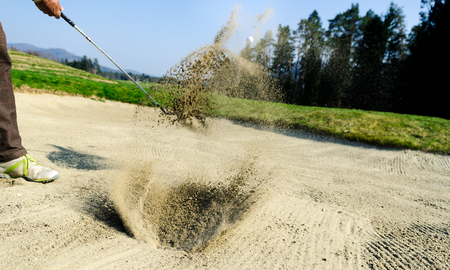 Golfer hitting out of a sand trap. The golf course is on the sand. Sand making splashesの写真素材