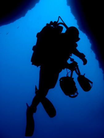 Silhouette of professional underwater photographer in front of underwater cave exit