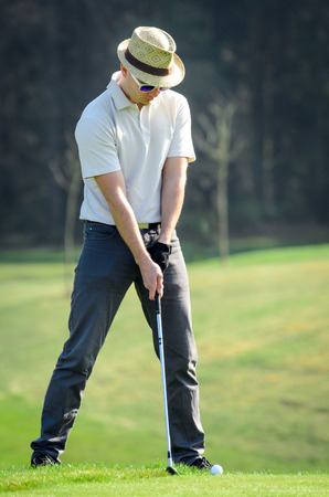 Golfer hitting golf shot with club on course putting on green while on vacation. Golfer is chipping a golf ball onto the green with driver golf clubの写真素材