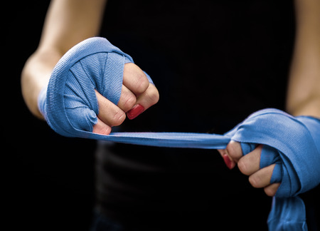 Woman is wrapping hands with blue boxing wraps. Self Defense for Women. Isolated on black with red nails. Strong hand and fist, ready for fight and active exerciseの写真素材