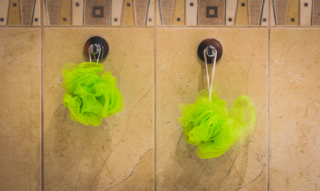 Two green bath sponges hanging from the bathroom wall. Bath accessories hanging from bathroom tiles.
