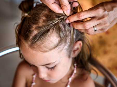 Mother is making of braids on little daughter's head. Hairdresser is braiding the hair on a young girl. Getting ready for school.の写真素材