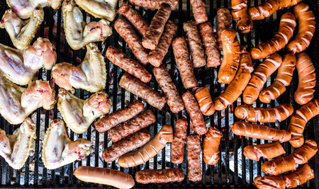 Mixed variety of Meat on barbecue grill with coal. Cevapcici, sausages, chicken wings and hot dogs on charcoal barbecue BBQ.の写真素材