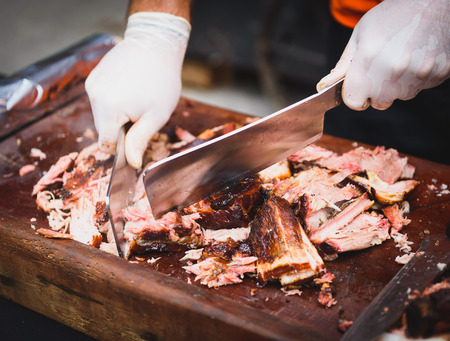 Chef Hands cutting Grilled spare beef or pork back ribs prepared in smoker with a hatchet. Delicious roasted cuts of meet made on barbecue smoker on a wooden cutting desk.の写真素材