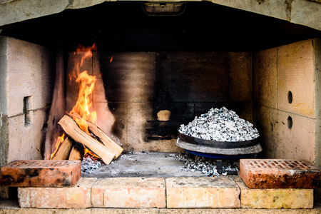 Cooking of traditional Balkan Greek Mediterranean Croatian meal Peka in metal pots called sac sach or sache or a metal lid. Fireplace with open fire and burning coals.の写真素材