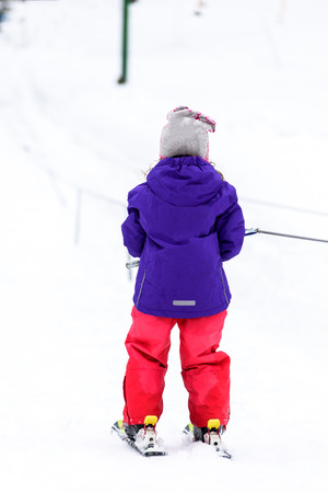 Little girl is learning to ski in ski resort. Child is using ski baby lift conveyor skiing for the first time. Active children are happy.の写真素材