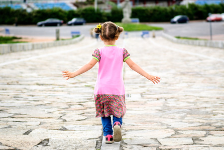 Little girl is running on stone paved promenade at Hercules Tower, a Coruna - Spain. Concept of freedom, childhood and national heritage.の写真素材