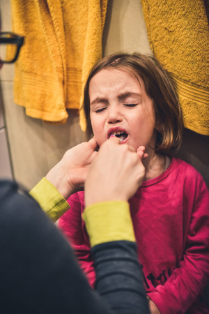 Little child is crying while mother brushes her teeth. The girl is not enjoying oral health care and bedtime brushing. The reality of children and mouth hygiene.の写真素材