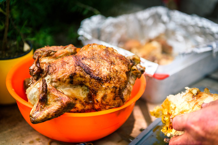 Crispy grilled rotisserie chicken in orange bowl at piknik party. Whole fried chicken is waiting to be cut or sliced outside in the nature.の写真素材