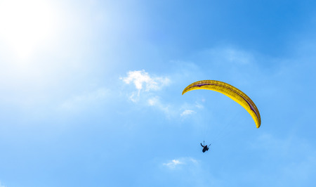 Paraglider flying against the blue sky with white clouds. Parachute on  a clear blue sunny day with sun and clouds.の写真素材