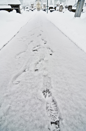 Foot steps in snow in cemetery and winter catholic church. Religious graveyard with tomb stones and a church in snowy winter and foot tracks made with boots or shoes.の写真素材