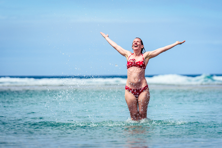 Woman enjoying the sea and waves of Atlantic ocean. Mature, mid aged, young attractive woman in bathing suit is walking in the ocean sea, playing and sprinkling the water. Atlantic ocean - Galicia, Spain.の写真素材