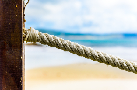 Rope fence on wooden pillar, sea and beach in background. A wooden fence with rope inlays on a sandy beach on Atlantic ocean in northern Spain.の写真素材
