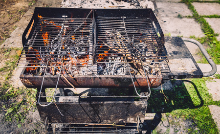 Burning and preheating old rusty barbecue grill cleaning dirty grid. Flames in bbq in nature - outdoors picnic. Preparing the barbecue for charcoal on backyard.の写真素材