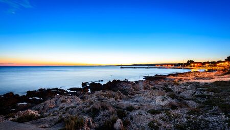 Sunset evening landscape photo of marine port of Silba Croatia. Long exposure photo of sunset, rocks on the shore and calm sea with fishing village in background. Mediterranean, Adriatic wallpaper background photo.の写真素材