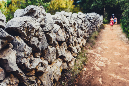 Stone rock fence wall gabion and family hiking in background. Old footpath and blurred family with children in background.の写真素材