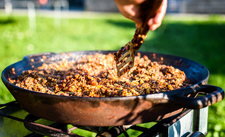 Cooking and making traditional Spanish Paella in iron cast pan. Preparing big paella outdoors on front yard party or business event. Professional catering buffet food.の写真素材