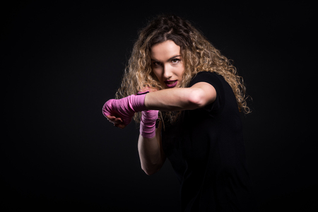 Fashion portrait of strong active kick boxing woman training. Attractive fit female is training martial arts and self defence for women. Shadow boxing with pink hand wraps isolated on balck background.の写真素材